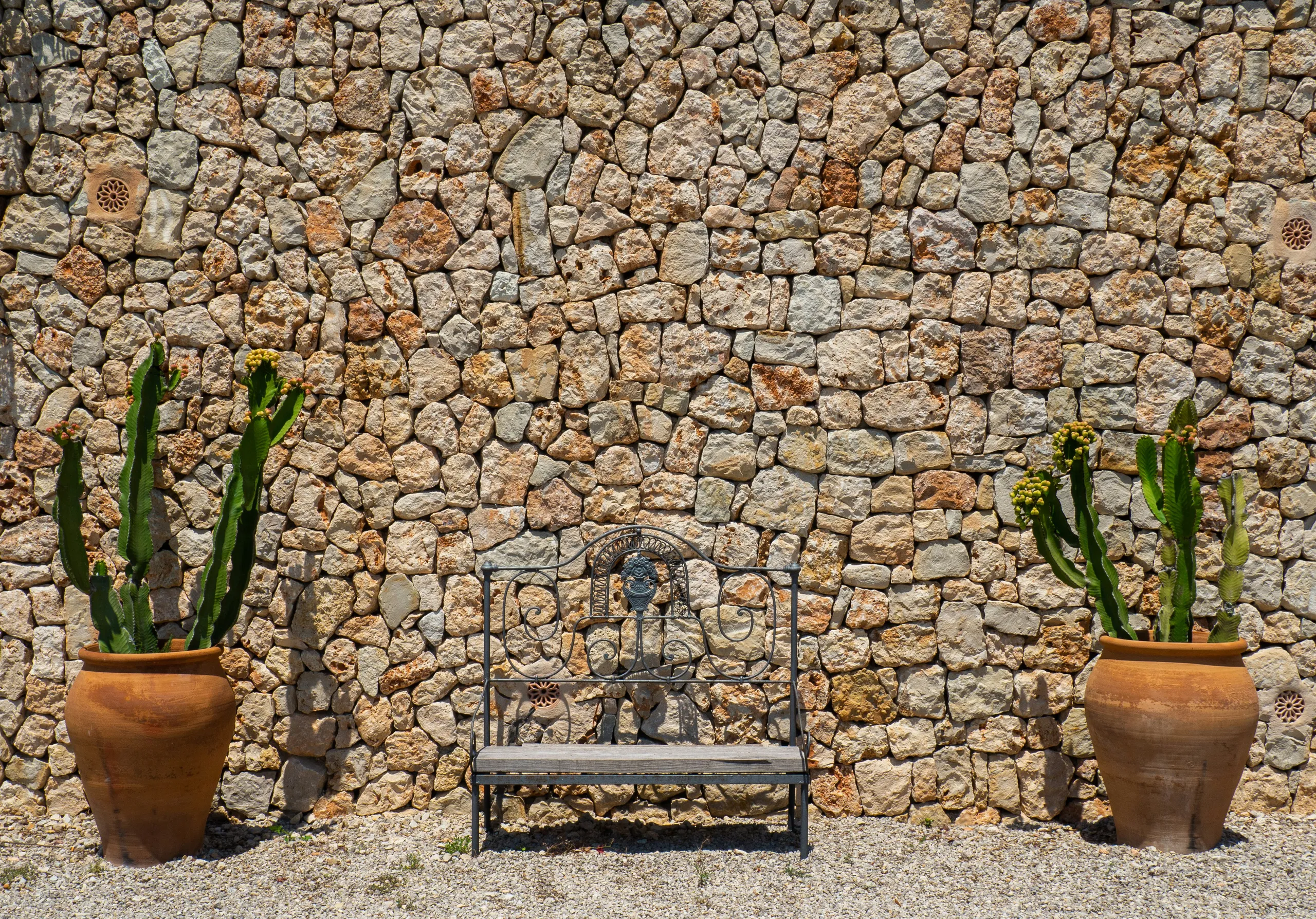 Muro de piedra con banco y olivos en macetas en la terraza