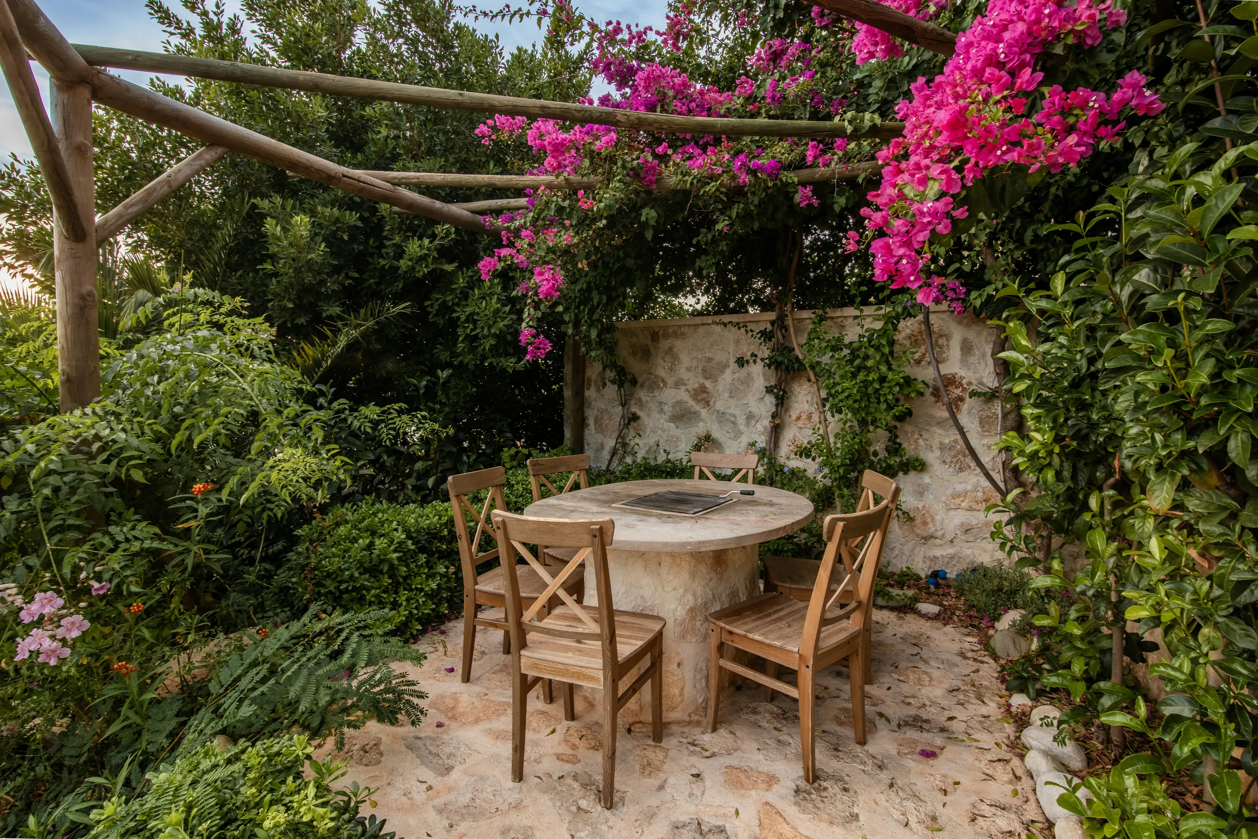 Patio íntimo con mesa de piedra bajo una pérgola cubierta de buganvilla en flor